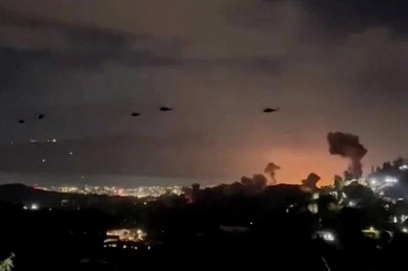 Helicopters fly past plumes of smoke rising from explosions, in Caracas, Venezuela, on Jan 3.