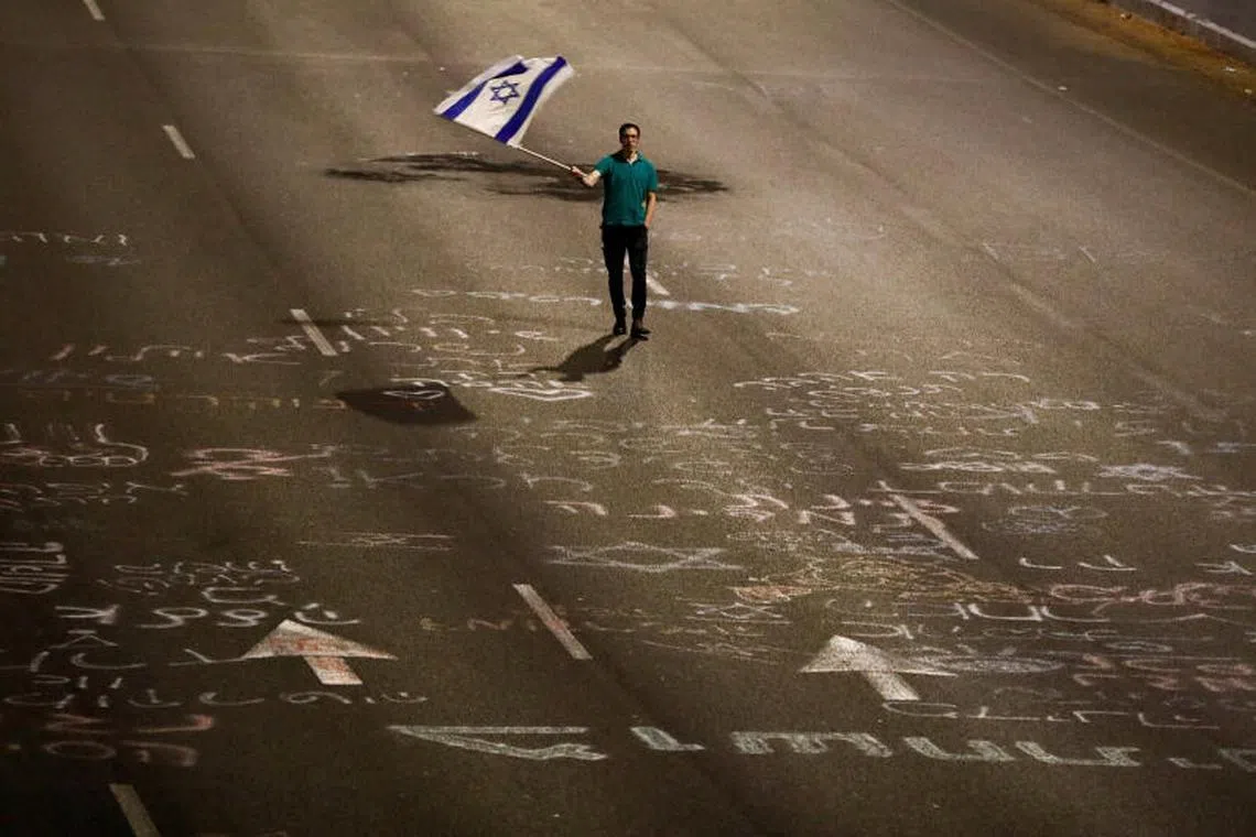 A man holds an Israeli flag, as protestors attend a right-wing demonstration in support of Israel's nationalist coalition government and its judicial overhaul, in Tel Aviv, Israel March on 30, 2023. 