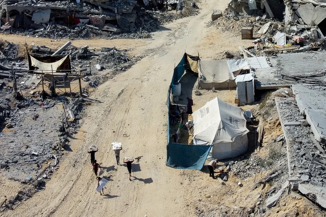Palestinians walk past a tent amid the rubble in a destroyed area, amid a ceasefire between Israel and Hamas in Gaza, in Gaza City. REUTERS/Dawoud Abu Alkas