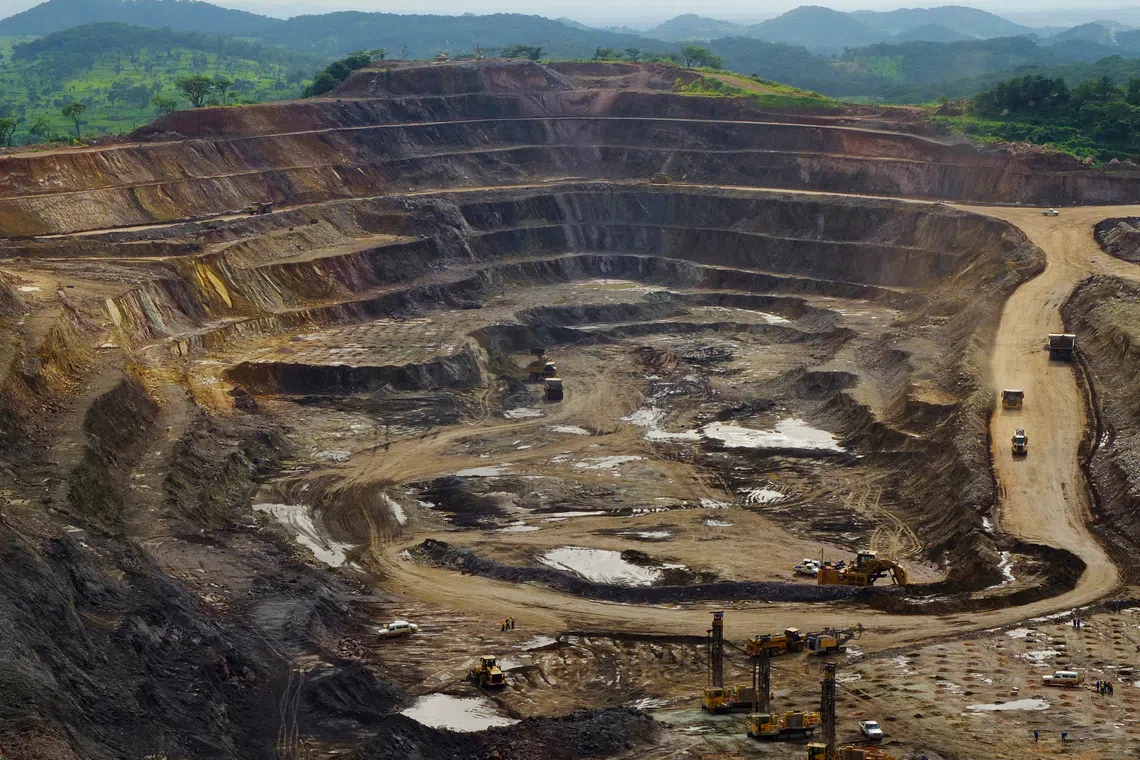 A large, terraced open-pit mine with heavy machinery under green hills.