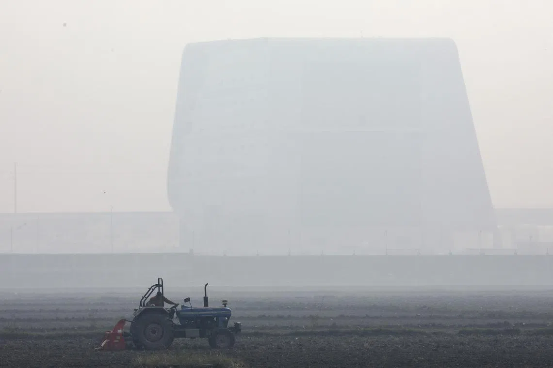 A farmer drives a tractor while working in a field as New Delhi is engulfed in heavy smog.