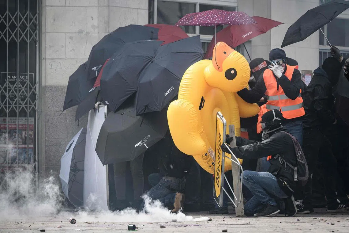 Protestors using umbrellas, road signs and inflatables as improvised shields as they face riot police amid clashes during a demonstration on May Day (Labour Day), to mark the international day of workers, more than a month after the government pushed an unpopular pensions reform act through parliament, in Nantes, northwestern France, on May 1, 2023. Opposition parties and trade unions have urged protesters to maintain their three-month campaign against the law that will hike the retirement age to 64 from 62. 
