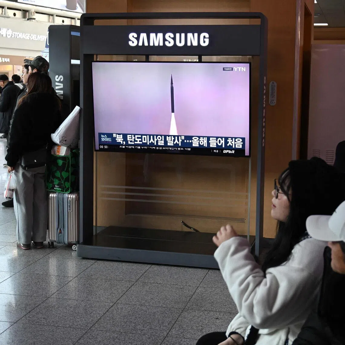 People sit in front of a television screen showing a news broadcast with file footage of a North Korean missile test, at a train station in Seoul on Jan 4, 2026.