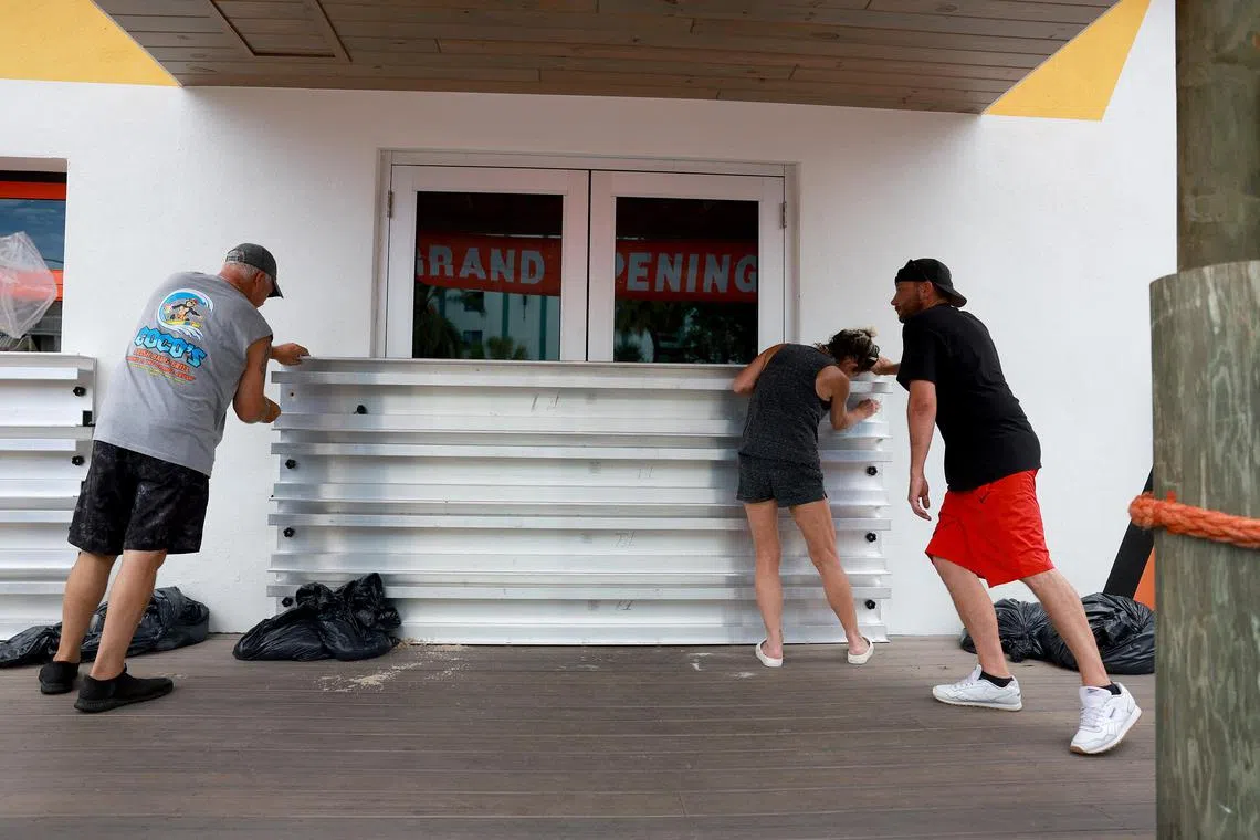 (From left) Steve Leitgeb, Michelle Fedeles, and Brandon Hadley place protective shutters over Coco's Crush Bar & Grill, in Indian Rocks Beach, Florida. ahead of Hurricane Idalia.