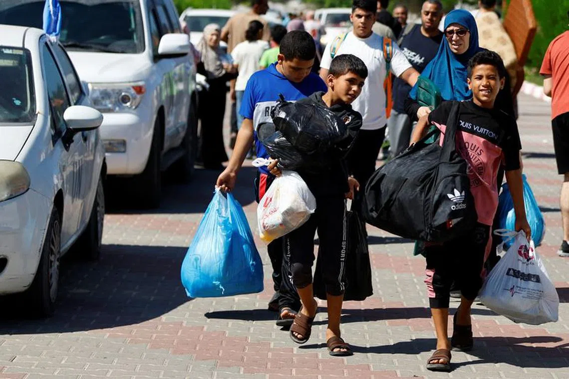 Families of staff of international organisations carry their belongings to shelter at a United Nations center after UNRWA said it relocated its central operations centre to the south of Gaza Strip after Israel's call for more than 1 million civilians in northern Gaza to move south within 24 hours, amid the Israeli-Palestinian conflict, in Khan Younis in the southern Gaza Strip October 13, 2023.  REUTERS/Ibraheem Abu Mustafa