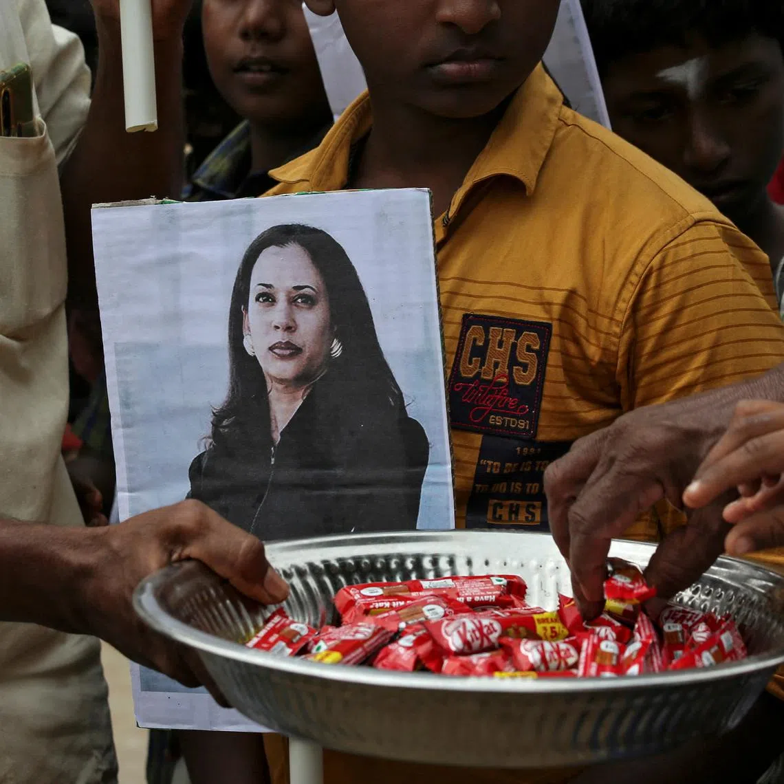 A man holds a placard with the photo of U.S. Vice President-elect Kamala Harris as another distributes sweets during the celebration on the day of her inauguration, in the village of Thulasendrapuram, where Harris' maternal grandfather was born and grew up, in the southern Indian state of Tamil Nadu, India, January 20, 2021. 