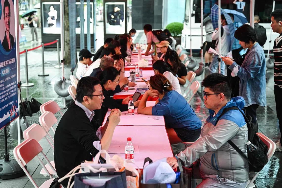 People visit a job fair in in Shanghai on May 31, 2024. At a job fair for soon-to-be graduates in central Shanghai on May 31, recruiters sat bored under washed-out tarpaulins as rain and an apparent lack of interest kept potential young employees away. (Photo by Hector RETAMAL / AFP) / TO GO WITH China-economy-politics-youth-unemployment,FOCUS by Rebecca BAILEY