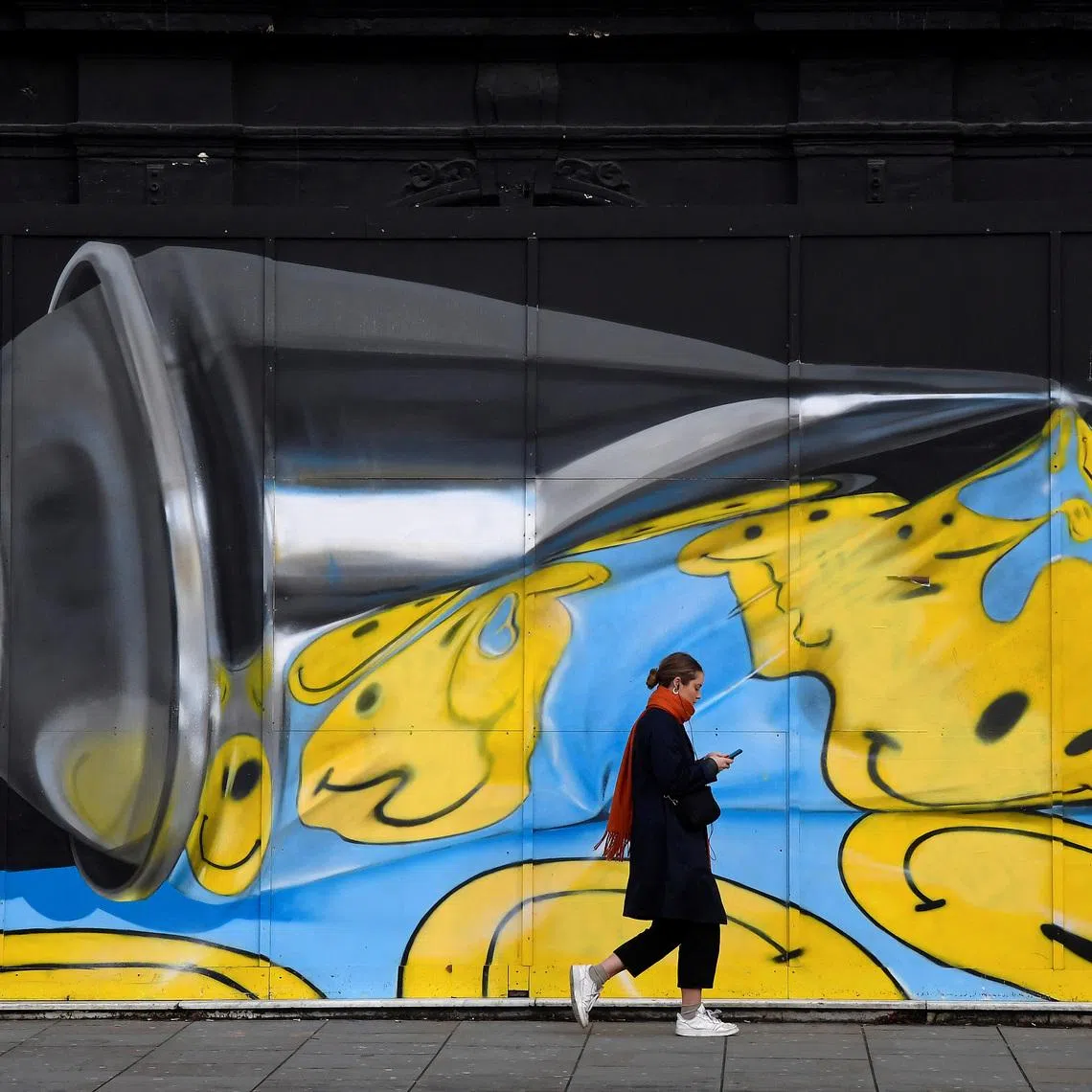 A woman views her phone as she walks past street art on a wall in London, Britain, December 18, 2019. REUTERS/Toby Melville
