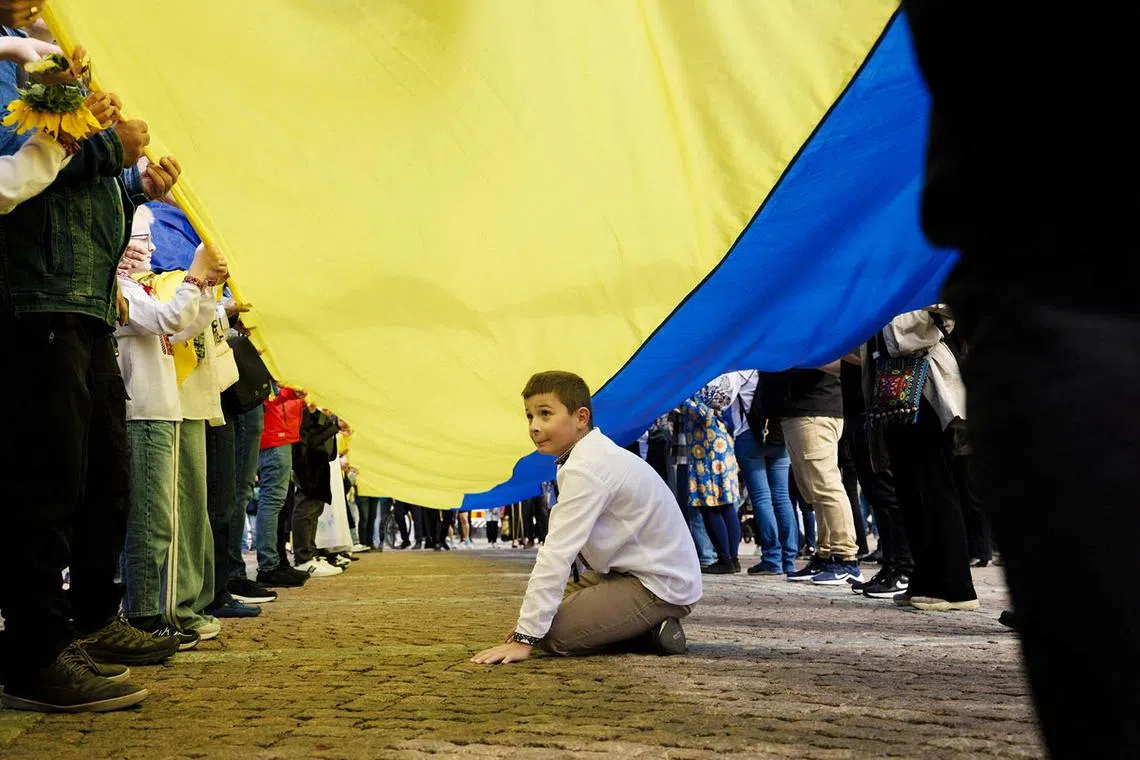 A boy sitting under a big Ukrainian flag during Ukraine's National Day festivities in Helsinki, Finland, Aug 24, 2025. 