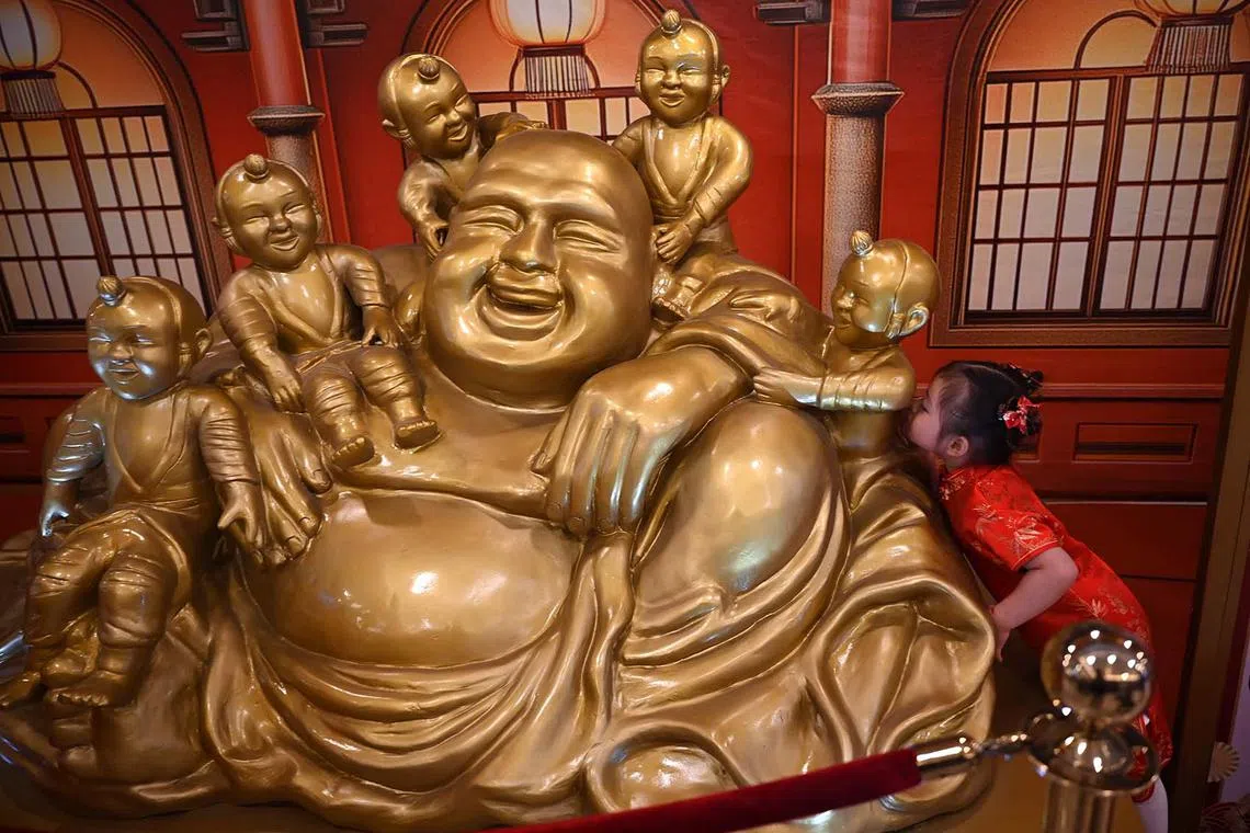 A young girl kisses one of the statues of a Buddha with children at a mall in Manila on January 24, 2025, ahead of the Lunar New Year of the Snake. (Photo by TED ALJIBE / AFP)