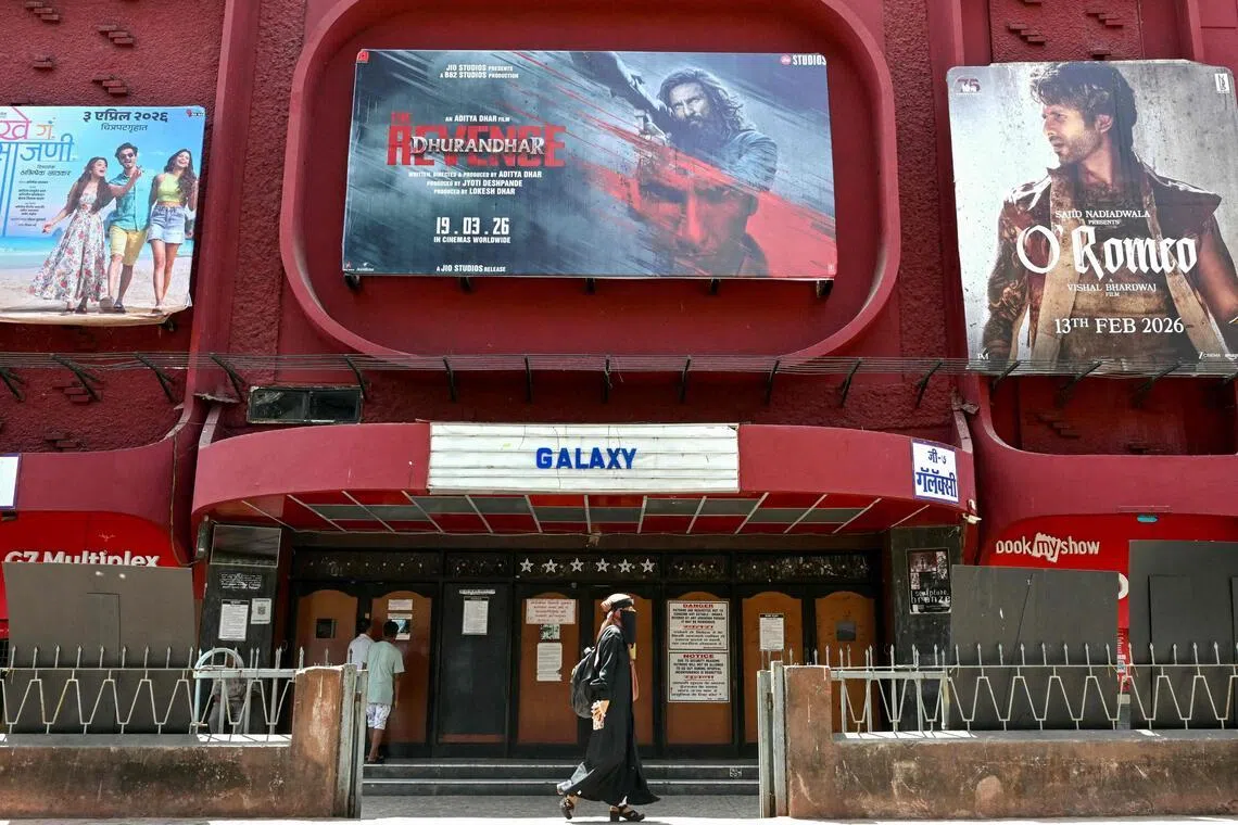 A woman walks past a poster of Indian Hindi-language spy action thriller film Dhurandhar: The Revenge (C), displayed outside a movie theatre in Mumbai on April 7, 2026. (Photo by Indranil MUKHERJEE / AFP)