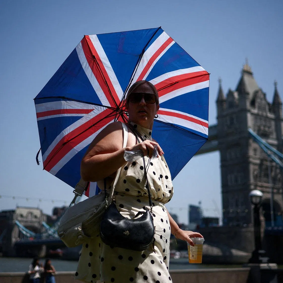 A woman uses an umbrella to shield herself from the sun while walking near Tower Bridge as Britain experiences record temperatures disrupting schools and transport networks, in London, Britain, June 25, 2026. REUTERS/Guglielmo Mangiapane