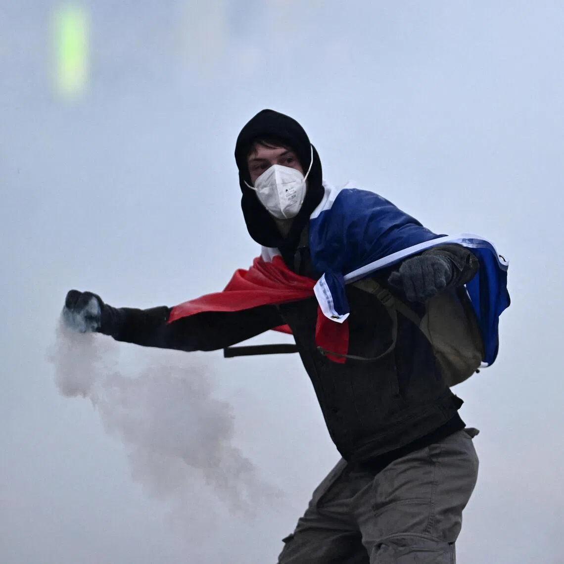 A masked protester wearing a French flag throws a tear gas canister in Paris on Oct 24.