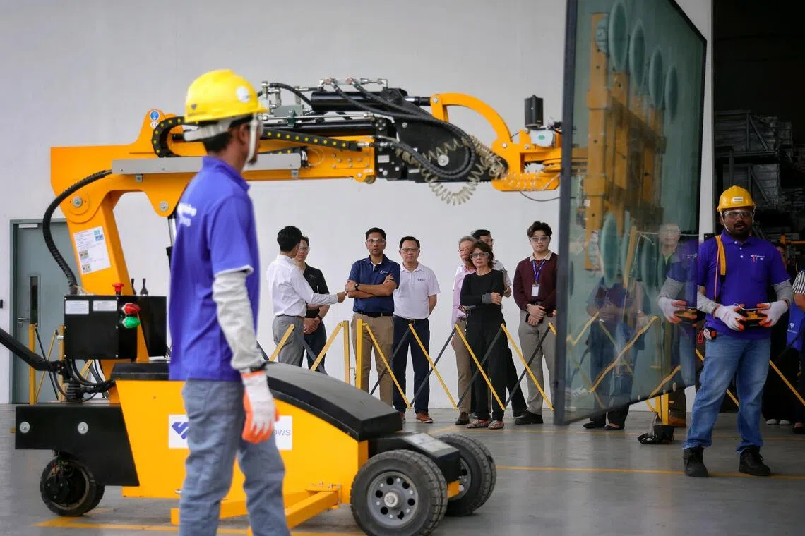 Minister of State for Ministry of Culture, Community and Youth and Ministry of Manpower Dinesh Vasu Dash (in dark blue top) looks on as workers (donning safety gloves) operate a glass lifting robot (which uses vacuum suction) during a tour of the factory and demonstration of good safety practices at Sapphire Windows in Loyang Drive on Sept 30, 2025. ST PHOTO: KEVIN LIM vcwsh30