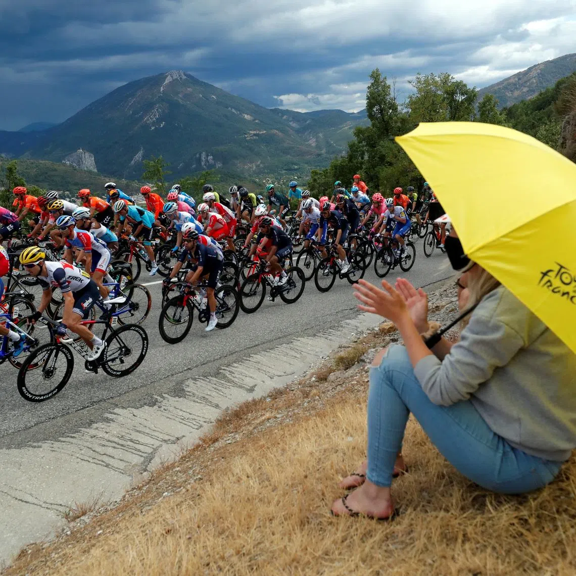 FILE PHOTO: Cycling - Tour de France - Stage 3 - Nice to Sisteron - France - August 31, 2020. A woman carries a yellow umbrella with the Tour de France logo as the peloton passes by. REUTERS/Stephane Mahe/ File Photo