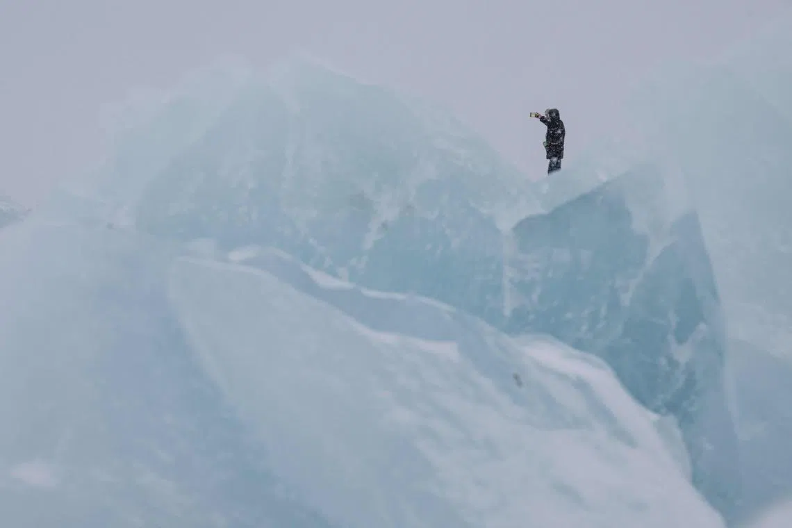 A man taking a picture as he walks along the shoreline past ice formations as snow falls in Nuuk, Greenland, on Jan 19, 2026. 