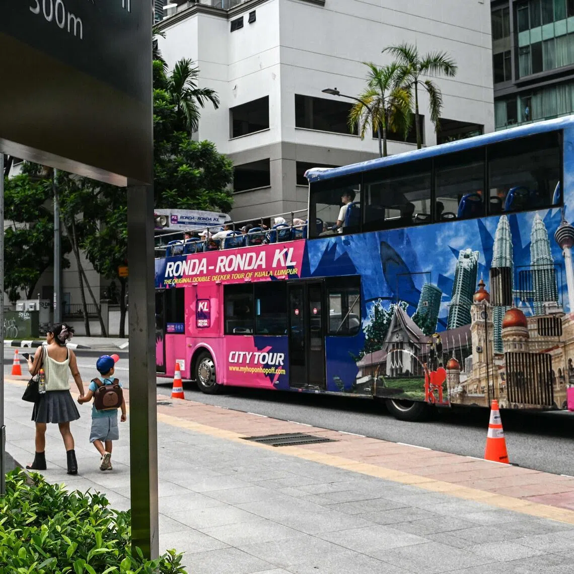 A woman walks with her son as a city tour bus passe by on a street in Kuala Lumpur on May 25, 2025.
