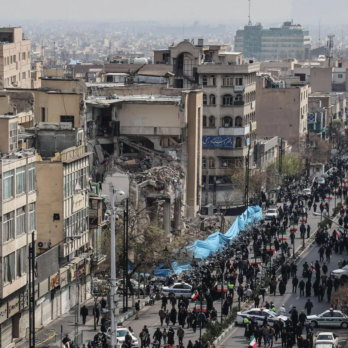 Iranians walking past a damaged building in Tehran, on March 11, during the funerals of military leaders and others killed in the US-Israeli attack on Iran.