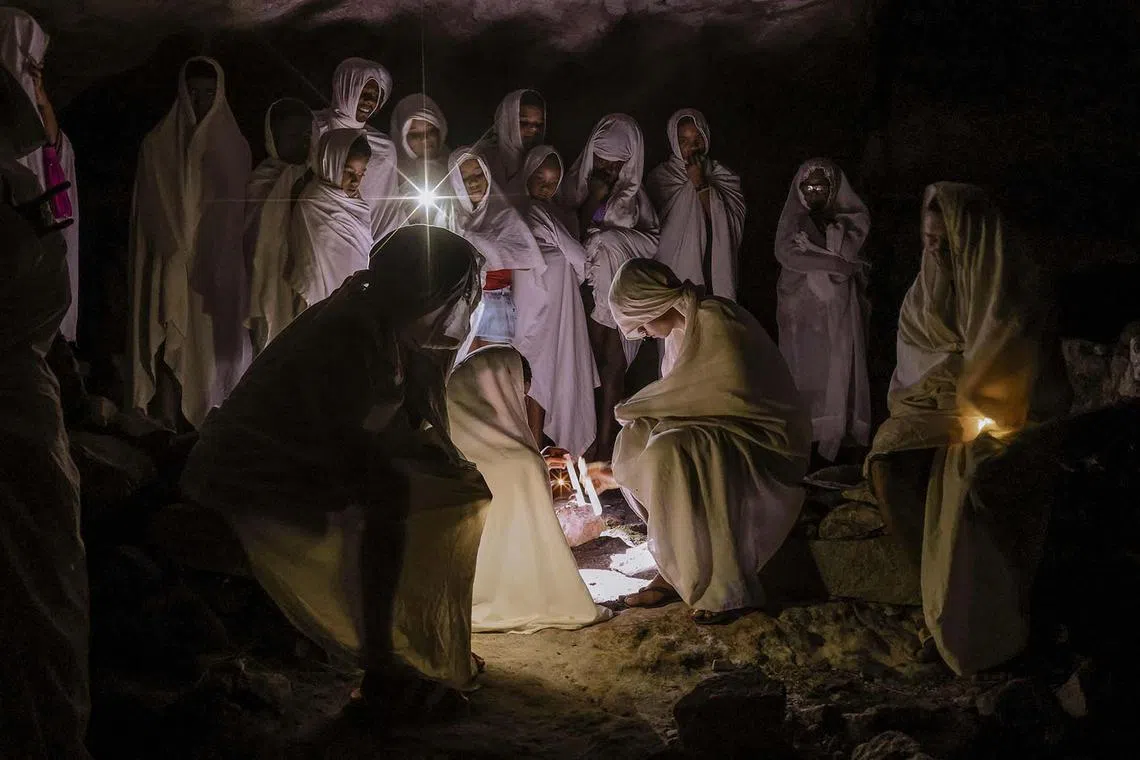 Catholic faithful dressed in white sheets lighting candles as they take part in the Terno das Almas procession in Igatu, a small town in the mountains of Chapada Diamantina National Park, Bahia State, Brazil, on April 15, 2025. Terno das Almas is an ancient ritual that takes place every night during Holy Week when participants make a pilgrimage through various parts of the village, praying and singing for the souls of their dead.