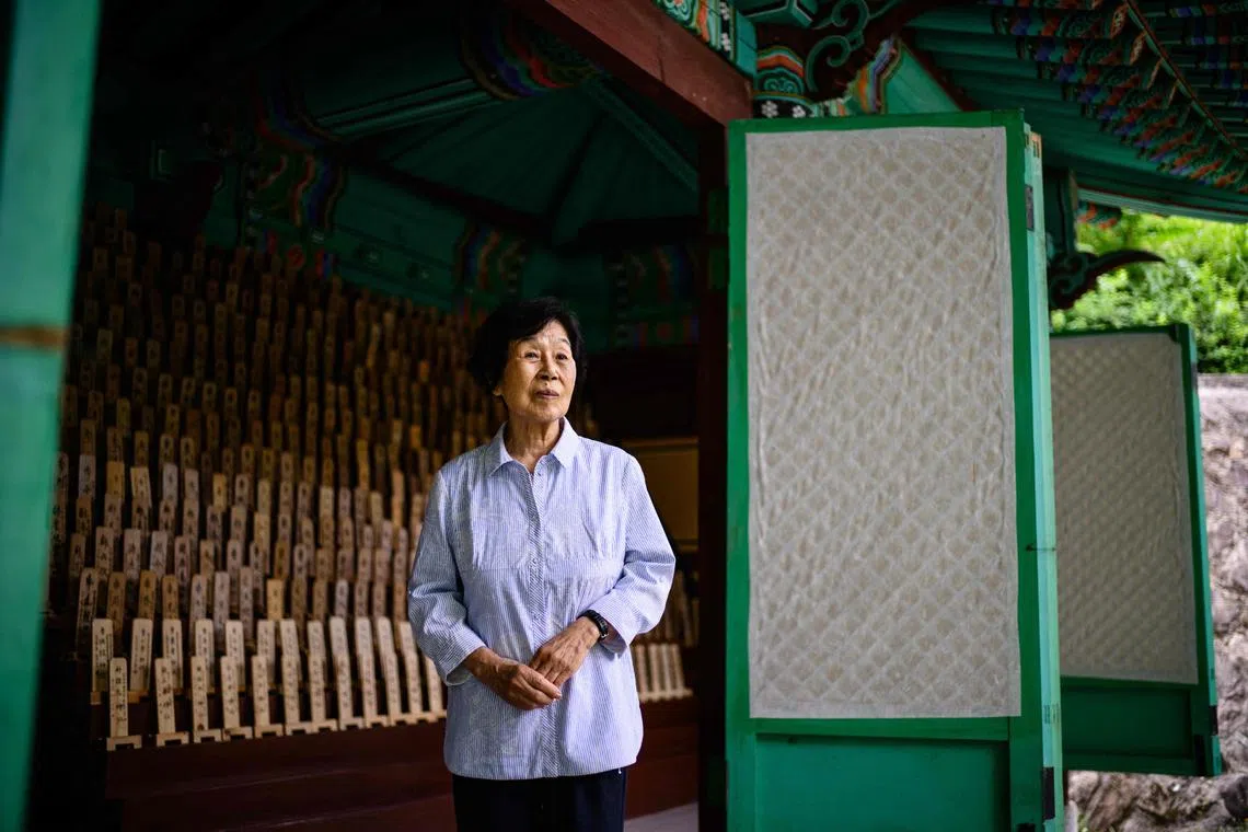 This photo taken in Hapcheon, South Gyeongsang, about 320 kilometres south of Seoul on July 10, 2025 shows Hiroshima atomic bomb survivor Bae Kyung-mi posing in front of a traditional structure holding 1,172 wooden plaques bearing the names of deceased victims  -- among them Bae’s three siblings -- behind the Hapcheon Atomic Bomb Victim Welfare Center, opened in 1996 by the Korean Red Cross with funding from both South Korean and Japanese governments, providing round-the-clock service to survivors of the World War II atomic bombings seeking help. Bae Kyung-mi was five years old when the Americans dropped "Little Boy", the atomic bomb that flattened Hiroshima on August 6, 1945. Some 740,000 people were killed or injured in the twin bombings of Hiroshima and Nakasaki which ended World War II -- and more than 10 percent of the victims were Korean, data suggests, the result of huge flows of people to Japan while it colonised the Korean peninsula. (Photo by Anthony WALLACE / AFP) / To go with Japan-SKorea-history-nuclear,FOCUS by Harumi Ozawa and Kang Jin-kyu
