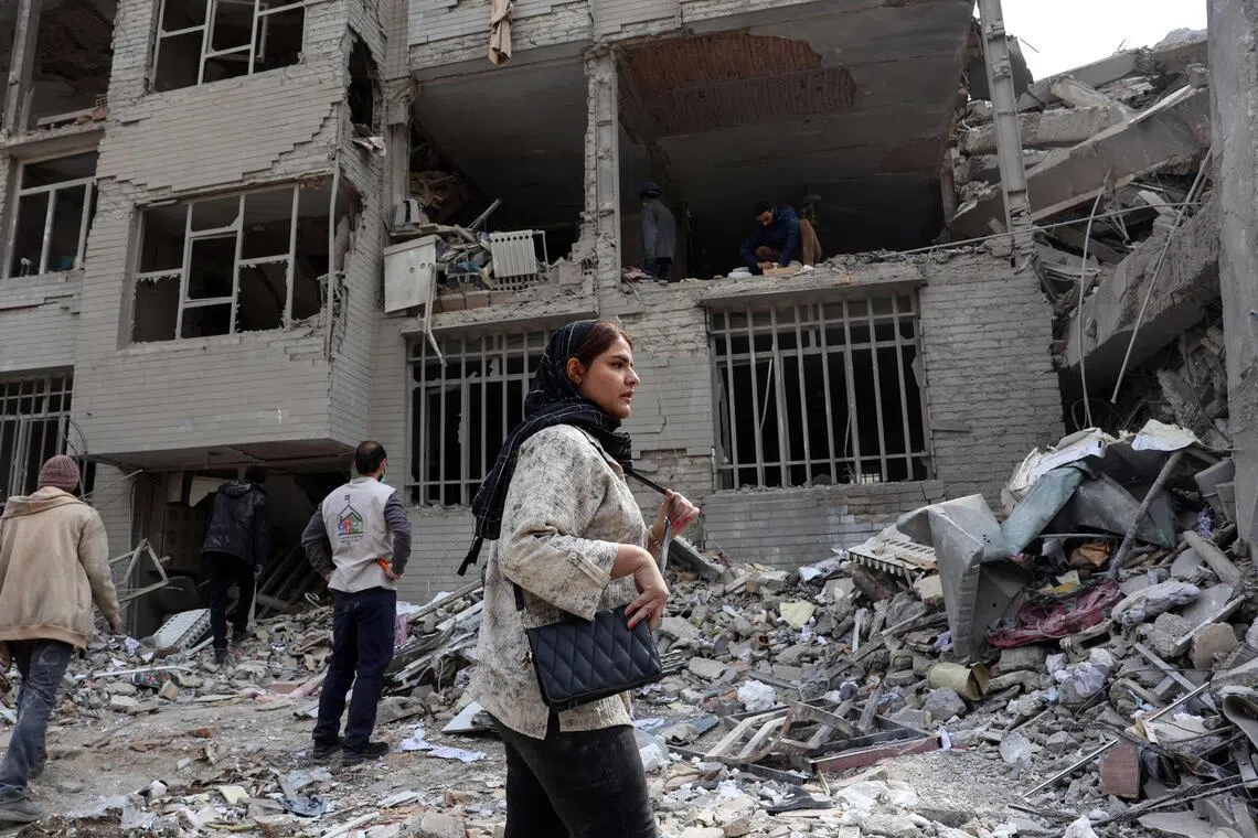 TOPSHOT - A woman stands in front of a destroyed residential building as residents collect their belongings from the rubble in Tehran on March 12, 2026. The United States and Israel started striking Iran on February 28, killing the Iranian supreme leader and top military leaders, and prompting authorities to retaliate with strikes on Israel and across the Gulf. (Photo by AFP) / 