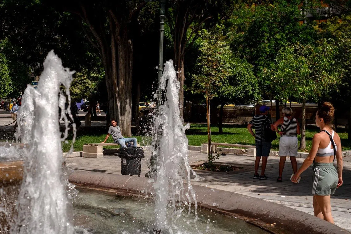 Tourists shelter in the shade of a tree near a water fountain during high temperatures on Syntagma Square in Athens, Greece.