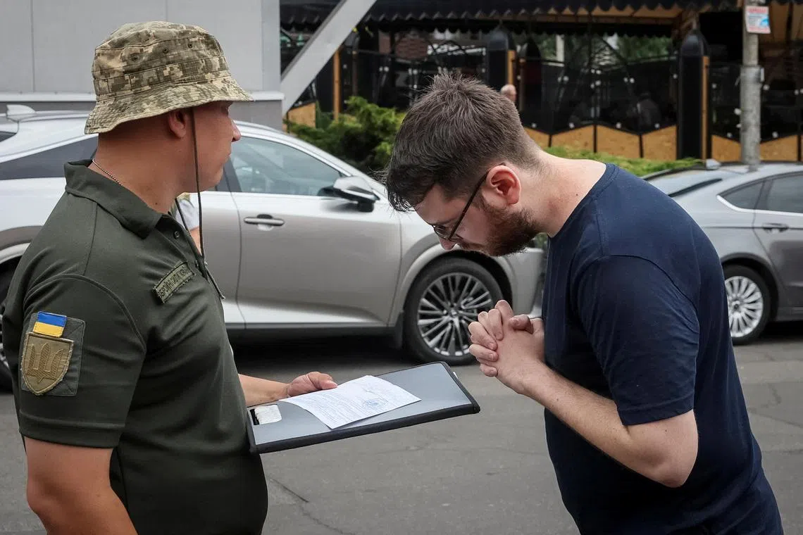 FILE PHOTO: A recruiting officer with the call sign 'Fantomas' speaks with a man on a street as he checks papers of men and hands out military summonses, amid Russia's attack on Ukraine, in Kyiv, Ukraine July 3, 2024. REUTERS/Gleb Garanich/File Photo