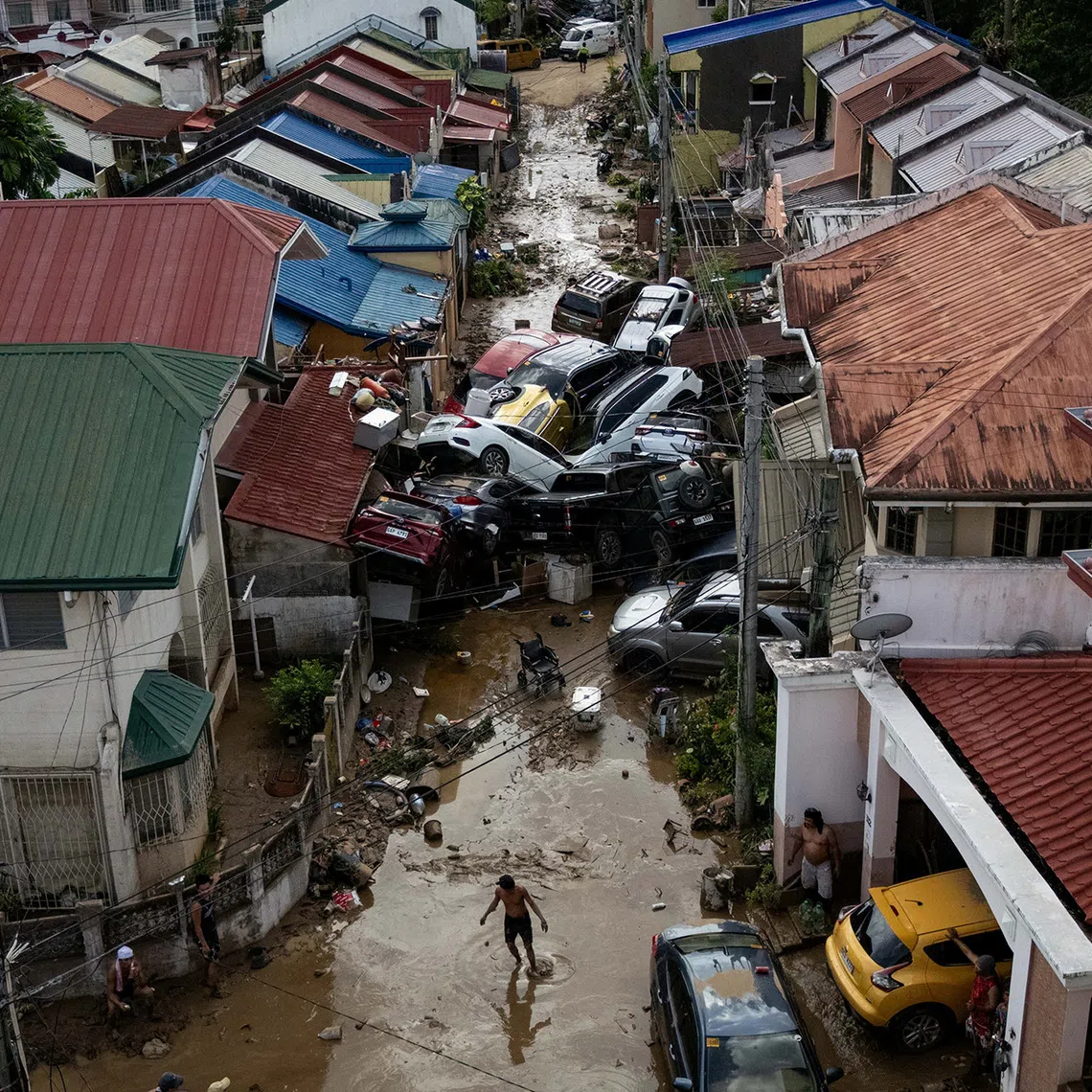 A man crosses a muddy street piled up with cars that were swept away in floods brought on by Typhoon Kalmaegi, in Bacayan, Cebu City, Philippines, on Nov 5, 2025. 