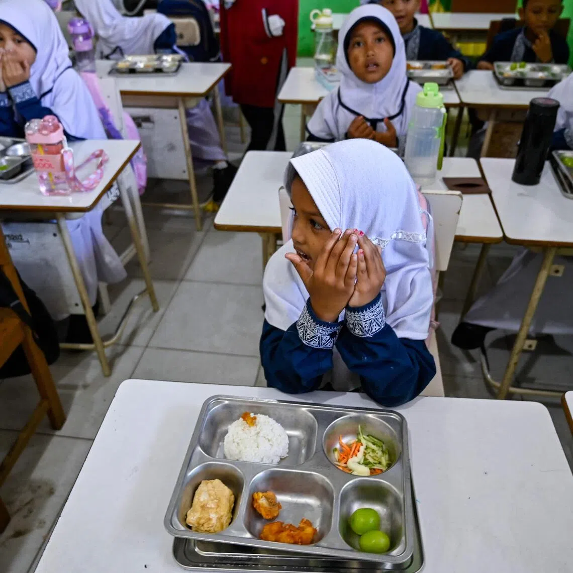 Students praying before eating meals supplied by the Indonesian government's free meal programme at an elementary school in Banda Aceh.