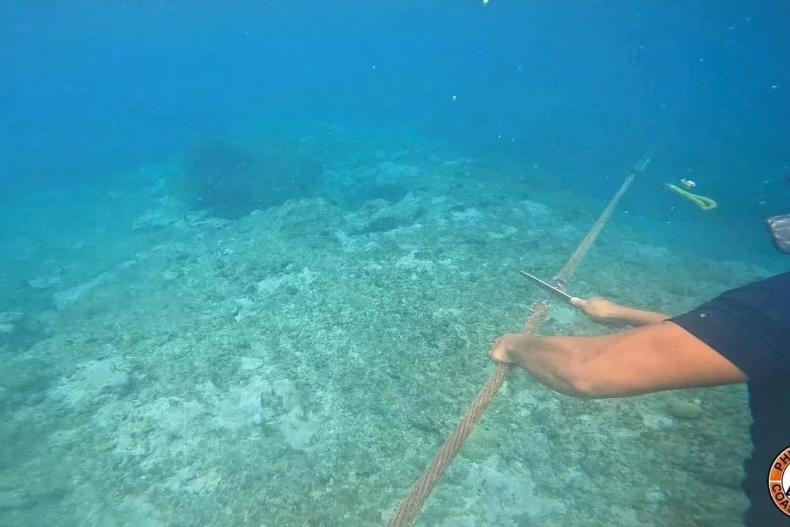 A Philippine Coast Guard personnel cuts the rope connecting the floating barrier that was installed near the Scarborough Shoal in the South China Sea.   