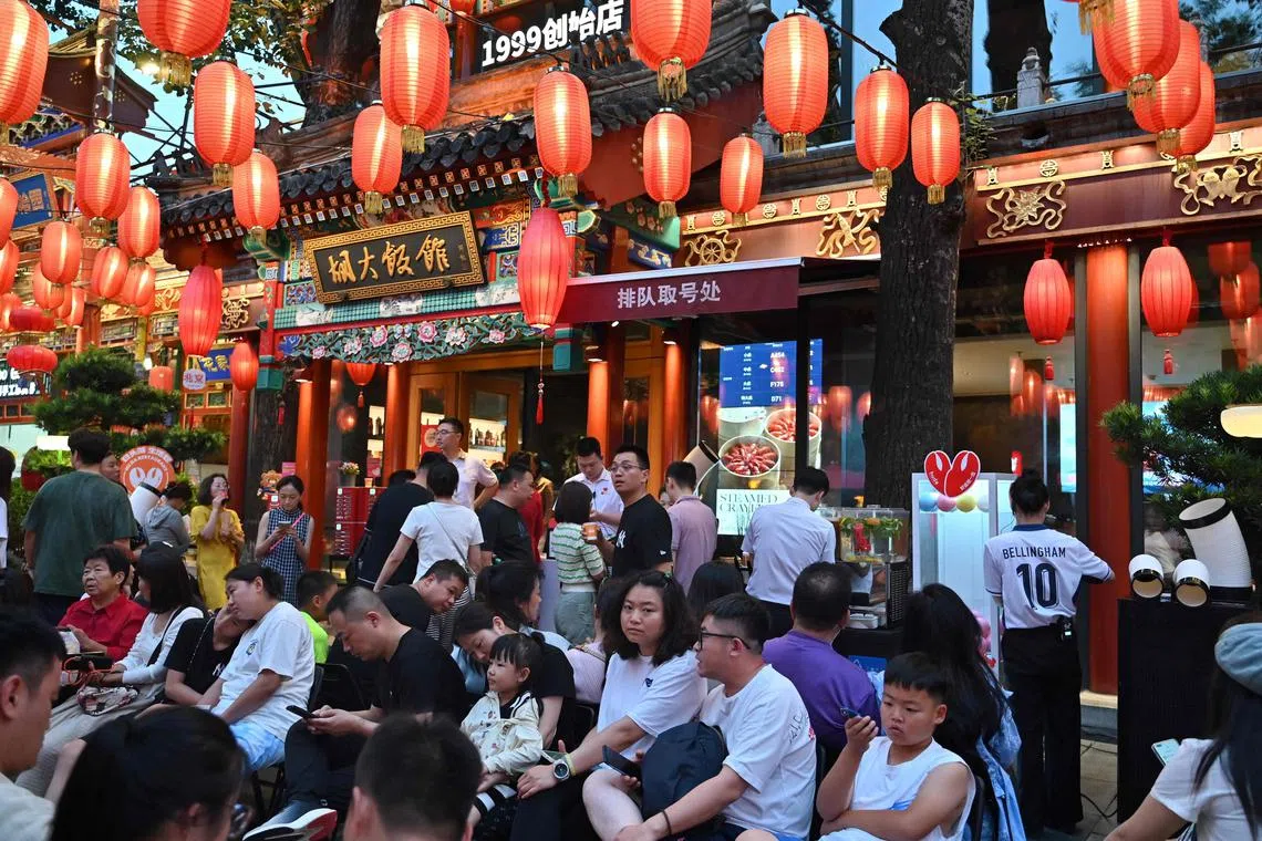 People wait outside under red lanterns for their turn to dine at a restaurant in Beijing on July 13, 2024.