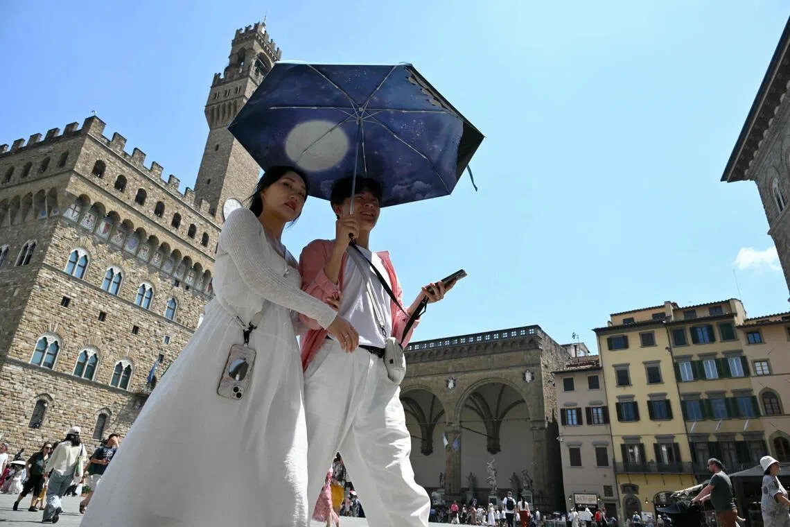 (FILES) A couple shields themselves from the sun under an umbrella as they walk through Piazza della Signoria in Florence during a heatwave on June 24, 2026. According to the the World Weather Attribution group of scientists, human-caused climate change is "unequivocally" responsible for the intensity of a record-breaking heatwave scorching Europe. It would have been "virtually impossible" for such exceptional temperatures to occur in June fifty years ago. (Photo by Alberto PIZZOLI / AFP)