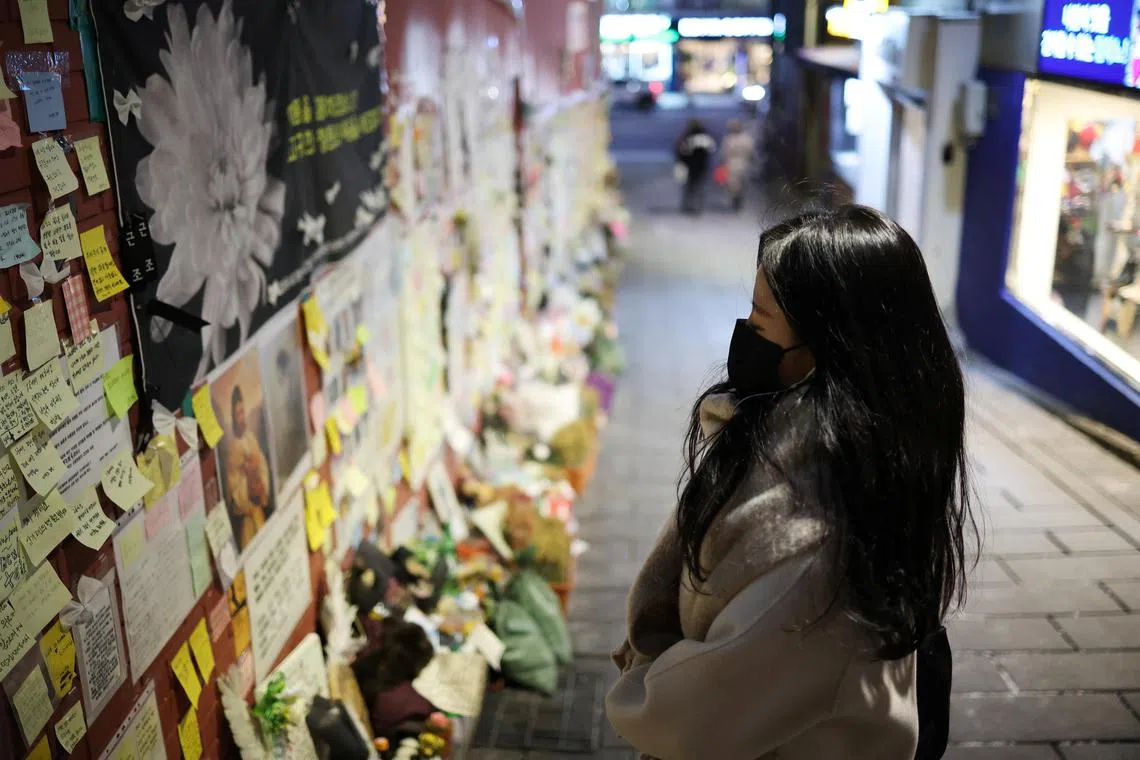 A woman prays while reading condolences messages attached to the wall of a narrow alley of Itaewon where the deadly Halloween crush that killed more than 150 in October happened, in Seoul, South Korea, December 18, 2022.  REUTERS/Kim Hong-Ji