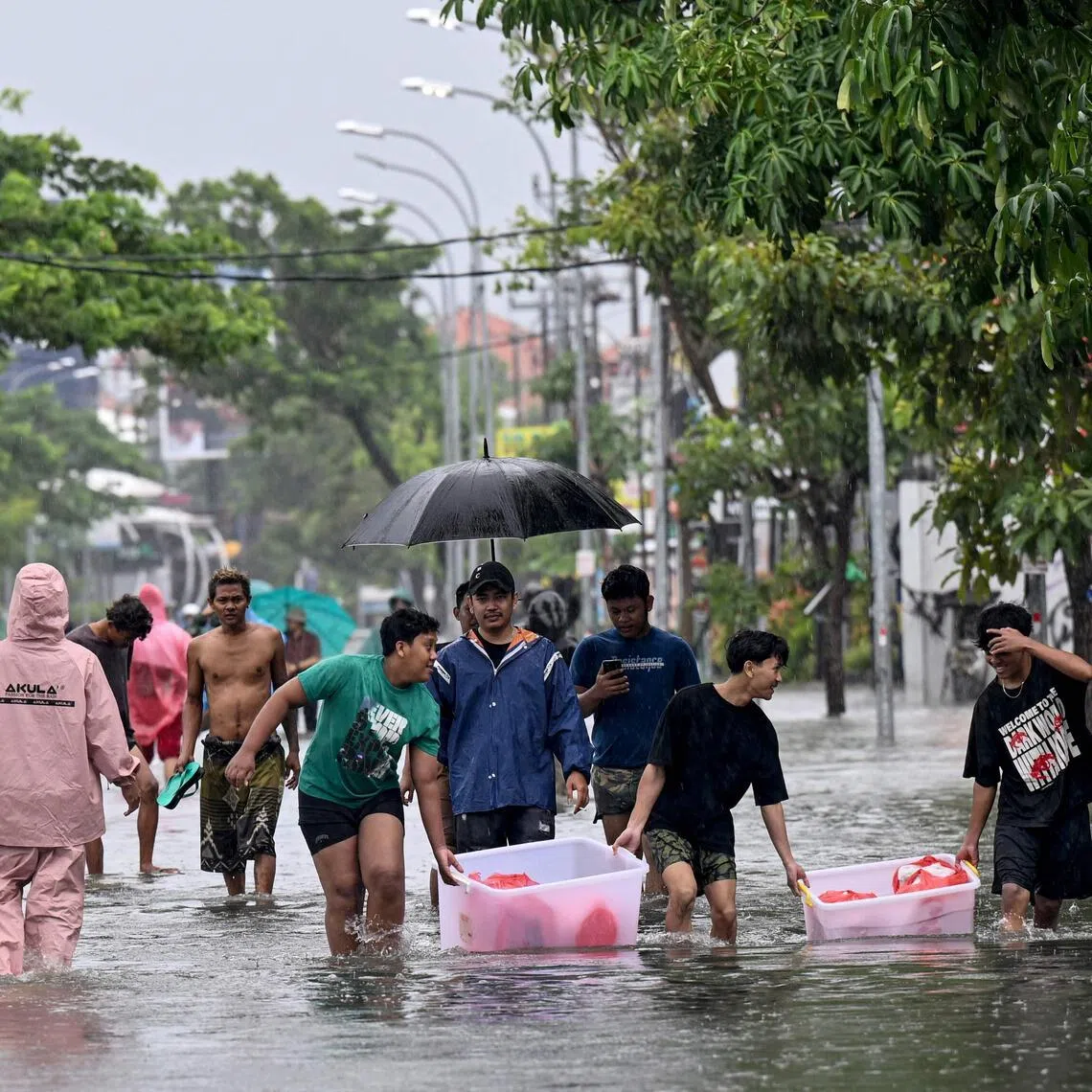 People move their belongings through the water on an inundated street amid floods following heavy rain at Legian Kuta near Denpasar on Indonesia's resort island of Bali on Feb 24, 2026. 