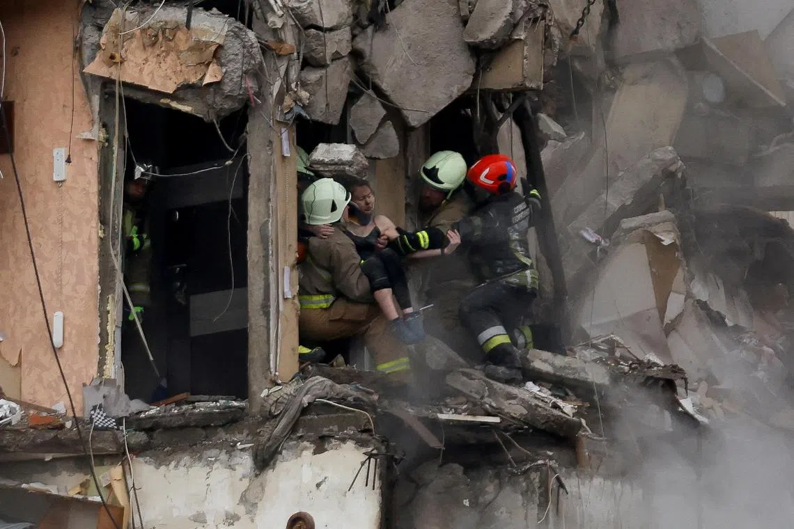 Emergency personnel evacuate a woman from an apartment block in Ukraine's Dnipro that was heavily damaged by a Russian missile strike.  