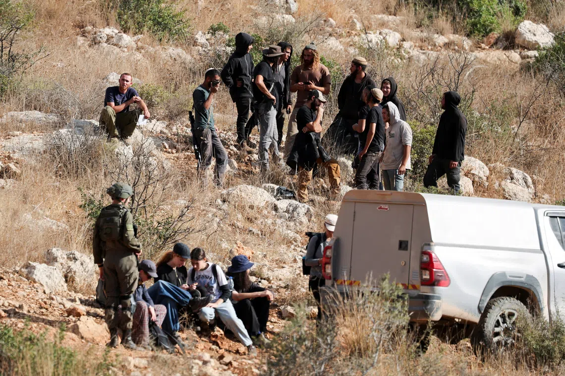 Israeli activists sit next to members of the Israeli forces on guard, as they prepare to pick olives during the harvest season at Palestinian-owned olive groves in Deir Abu Mashal, near Ramallah, in the Israeli-occupied West Bank, October 19, 2026. REUTERS/Ammar Awad