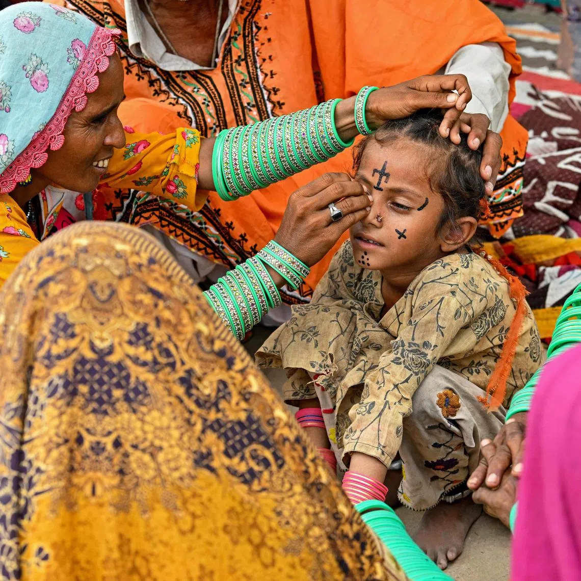 Artist Guddi Manthar (L), drawing an indigenous tattoo on seven-year-old Champa's face at the Jogi Colony in Umerkot.