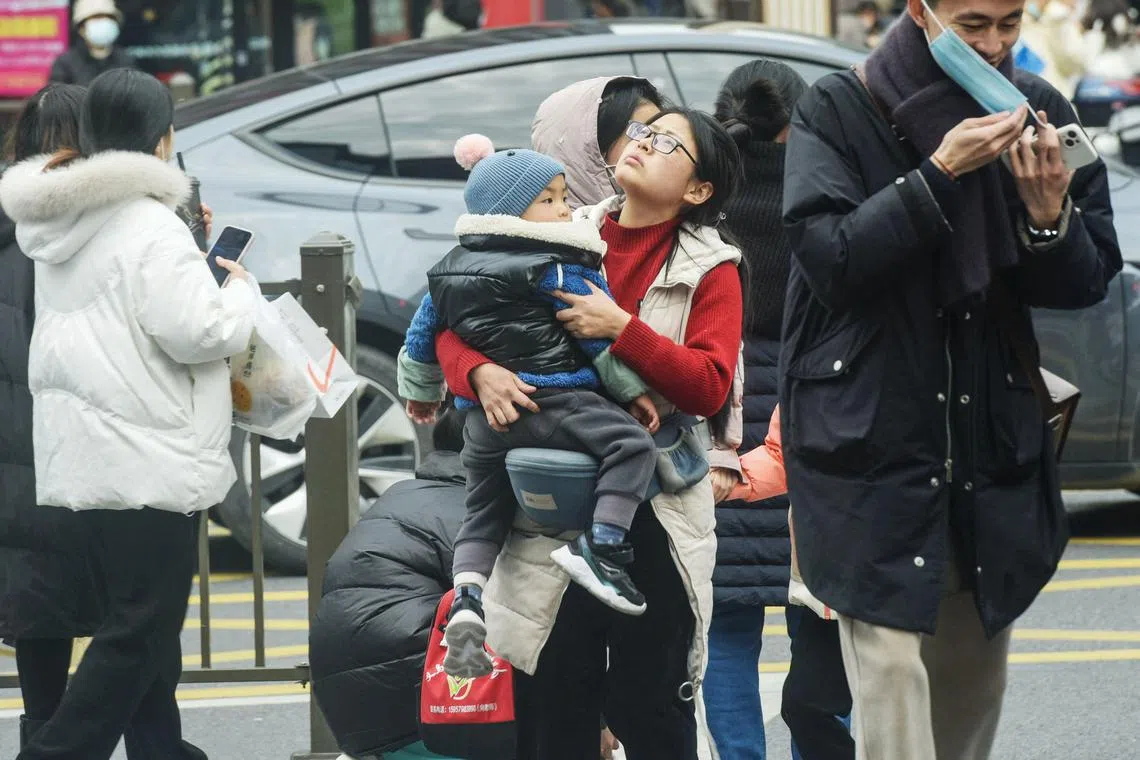 A woman holding a child as she walks across a street in Hangzhou, in China's eastern Zhejiang province.  China's population shrank last year for the first time in more than six decades.