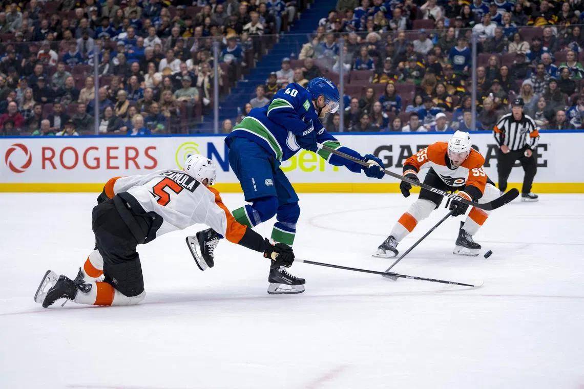 Philadelphia Flyers defenseman Egor Zamula and defenseman Rasmus Ristolainen stick check Vancouver Canucks forward Elias Pettersson during a National Hockey League game.