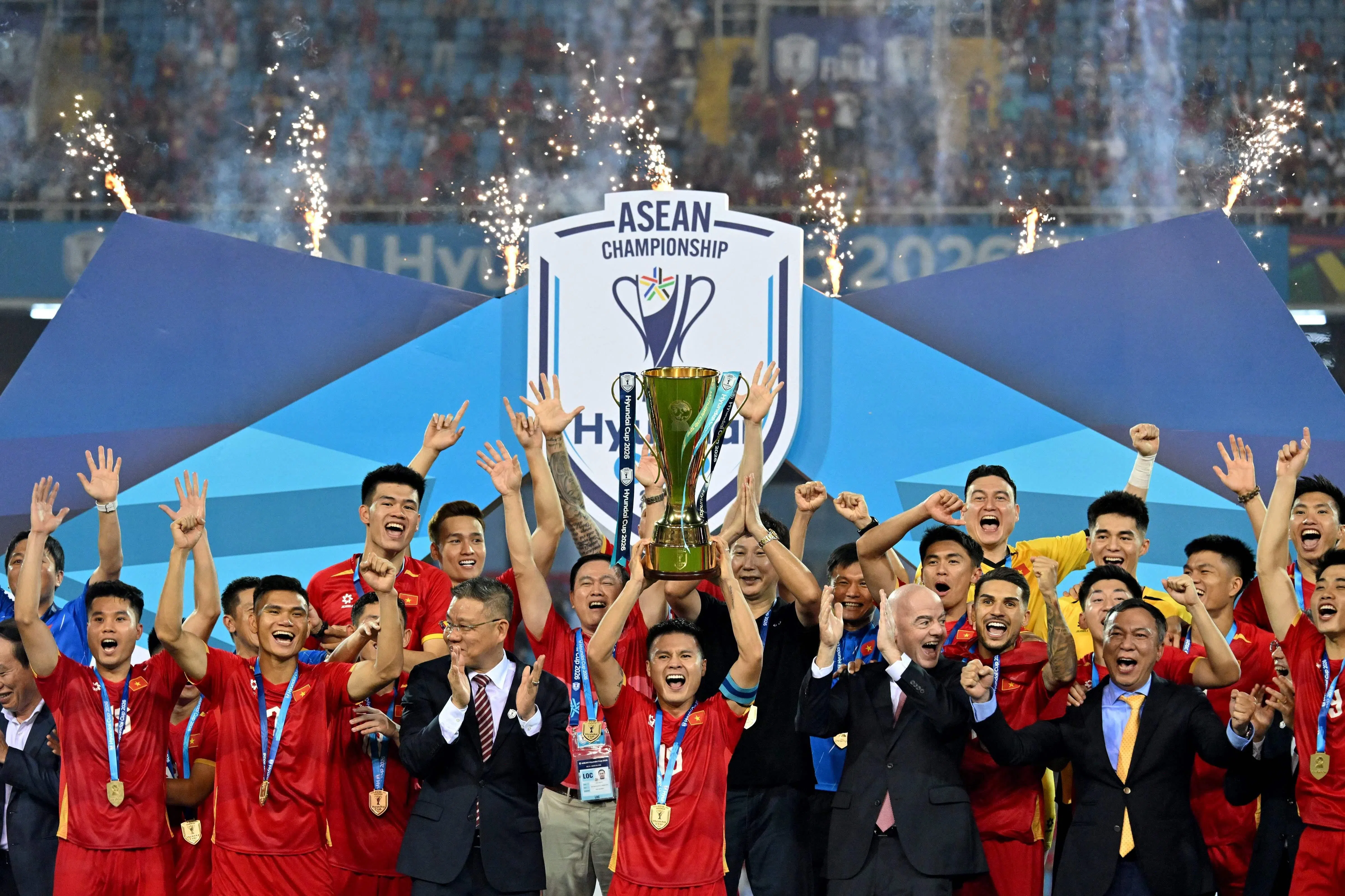 Vietnam's Captain Nguyen Quang Hai (C) lifts the ASEAN Cup Winner's Trophy alongside FIFA President Gianni Infantino (CR) and teammates after winning the ASEAN Championship Cup 2026 match between Vietnam and Thailand in My Dinh National Stadium in Hanoi on August 26, 2026. (Photo by Nhac NGUYEN / AFP)