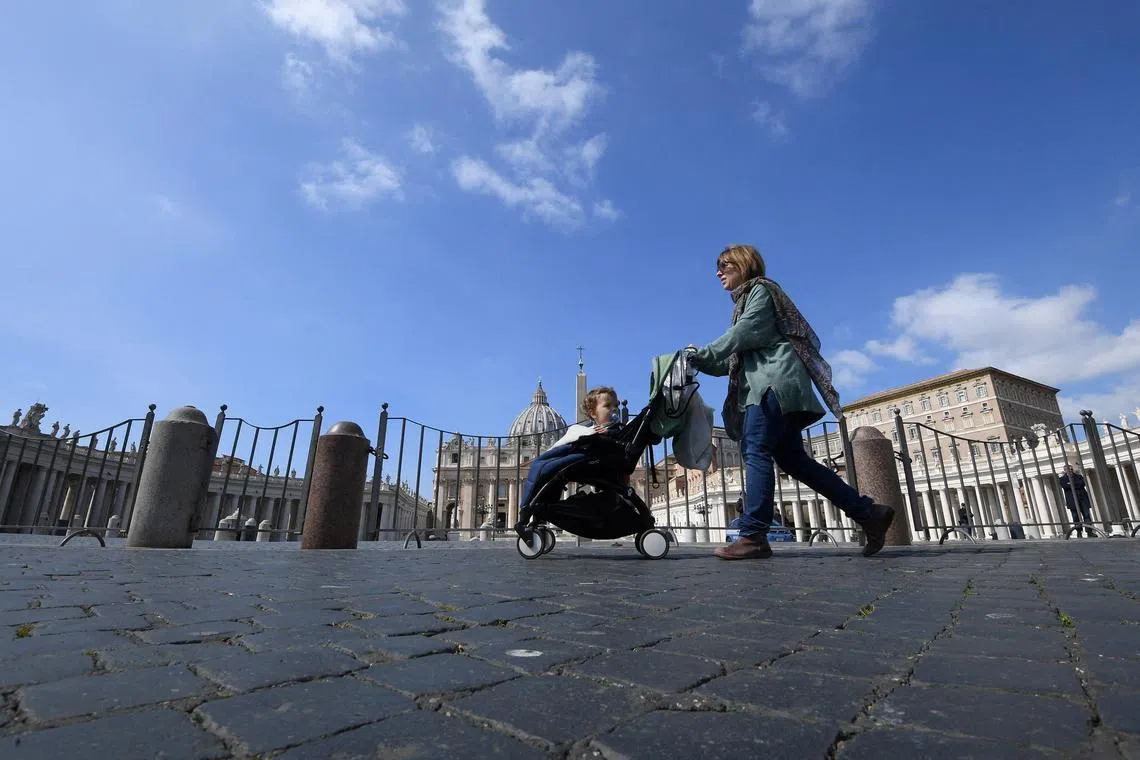 FILE PHOTO: A woman with a child in a pram walks past the St. Peter's Square, on the sixth day of an unprecedented lockdown across of all Italy imposed to slow the outbreak of coronavirus in Rome, Italy March 15, 2020. REUTERS/Alberto Lingria/File Photo
