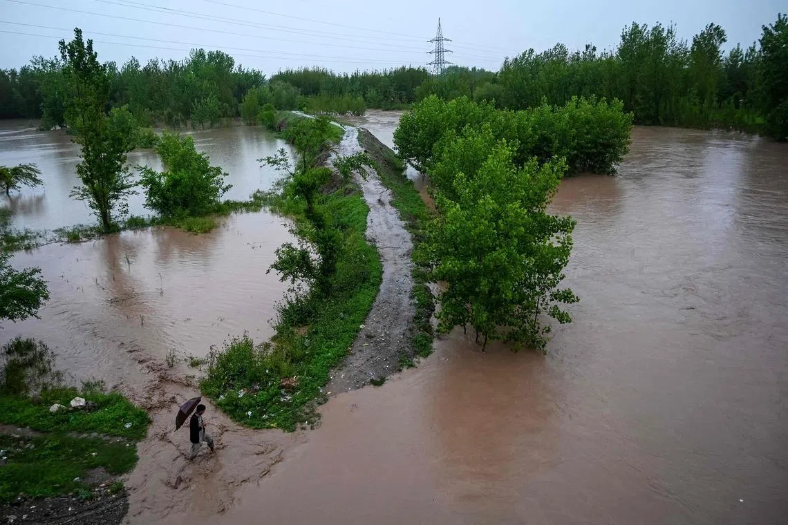A man walking along a flooded path as torrential rains cause water channels to overflow, inundating nearby areas of Peshawar in Pakistan, on April 7, 2026. 