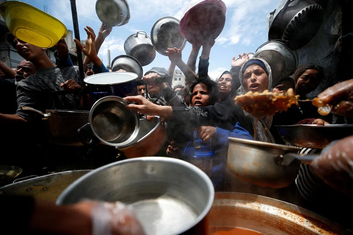 FILE PHOTO: Palestinians wait to receive food cooked by a charity kitchen, in Beit Lahiya, northern Gaza Strip, April 28, 2025. REUTERS/Mahmoud Issa/File Photo