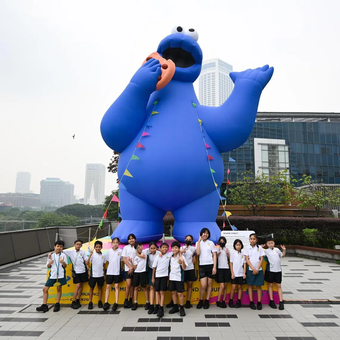 Beneficiaries of The Straits Times School Pocket Money Fund posing in front of a 7m-tall Cookie Monster at the level three rooftop garden.