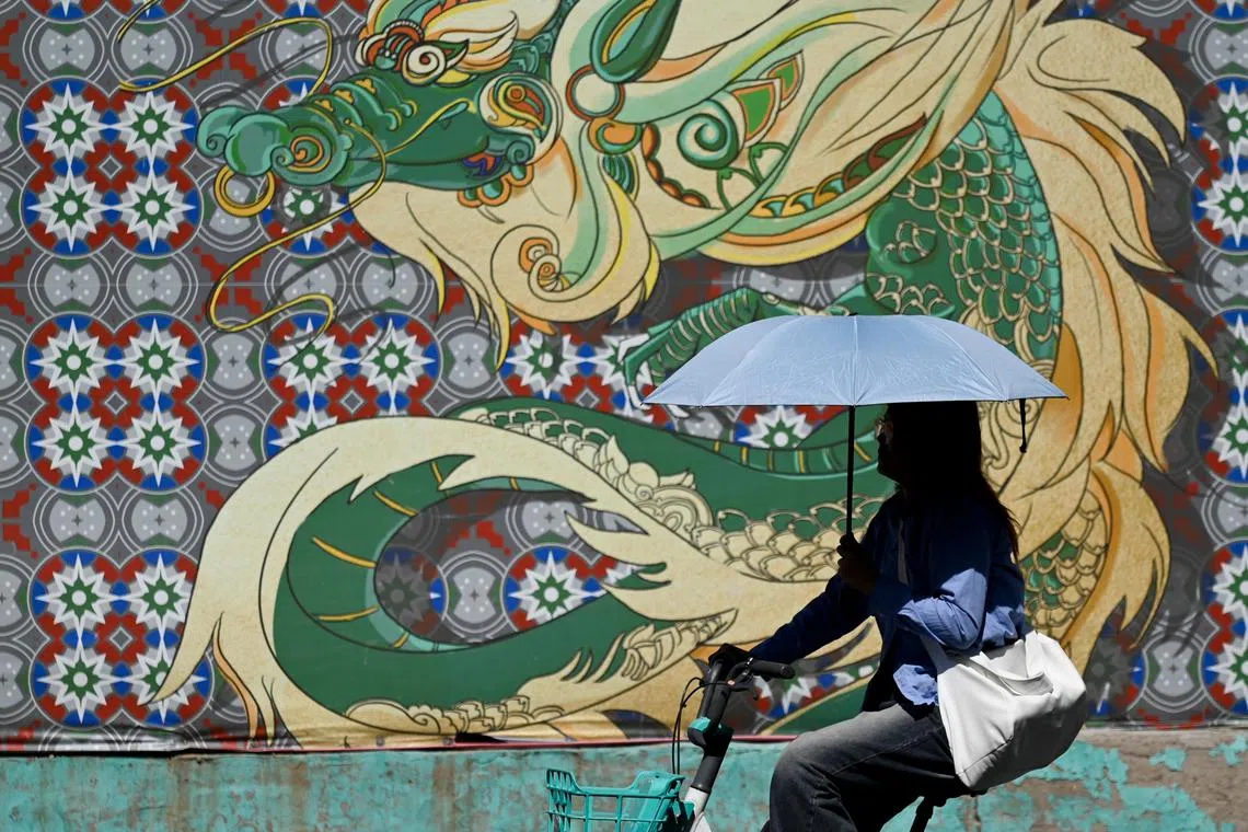 A woman sheltering herself from the sun with an umbrella as she rides a bicycle along a street on a hot day in Beijing, on June 12, 2024.