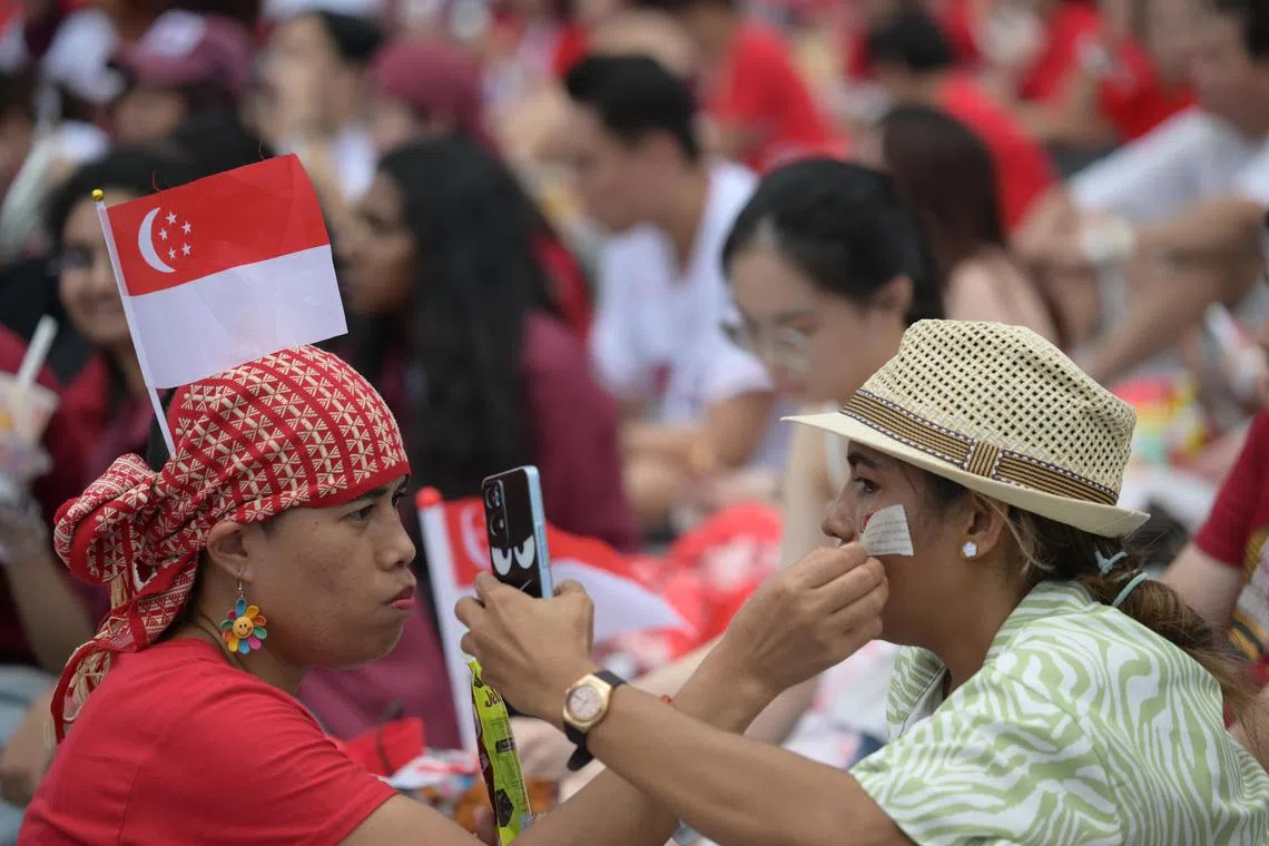 A spectator helping to apply a temporary face tattoo on her friend at The Promontory @ Marina Bay on Aug 9. Nearly 7,000 people gathered at the location to watch the synchronised NDP live show.