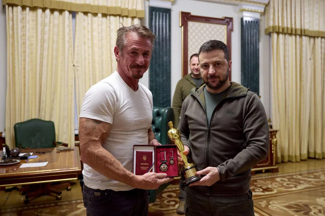 This handout picture taken and released by Ukraine's presidential press-service on Nov 8, 2022 shows the Ukrainian President Volodymyr Zelensky (right) posing with US actor Sean Penn after receiving latter's Oscar statuette and handing him the Order of Merit, III degree during their meeting in Kyiv. 