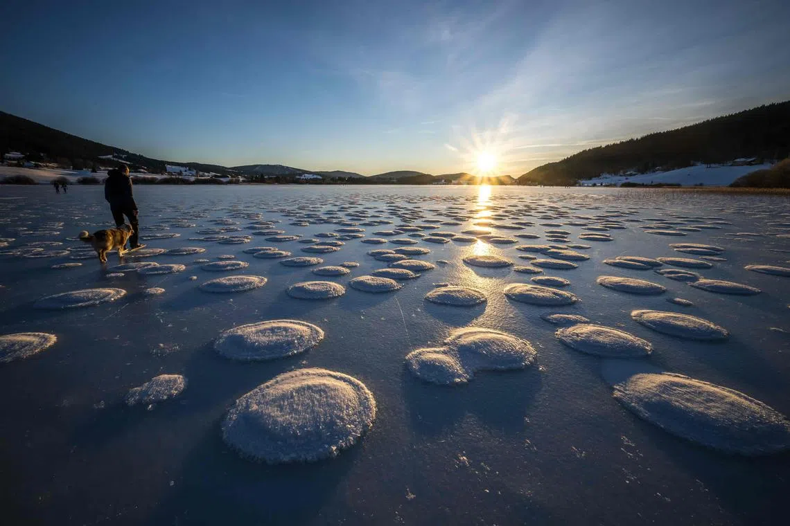 Strollers walk between pancakes snow on the frozen Lake des Rousses in Les Rousses, central-eastern France, on Jan 1, 2025. This phenomenon forms when slushy ice in water clumps into round, pancake-like shapes due to waves or currents. 