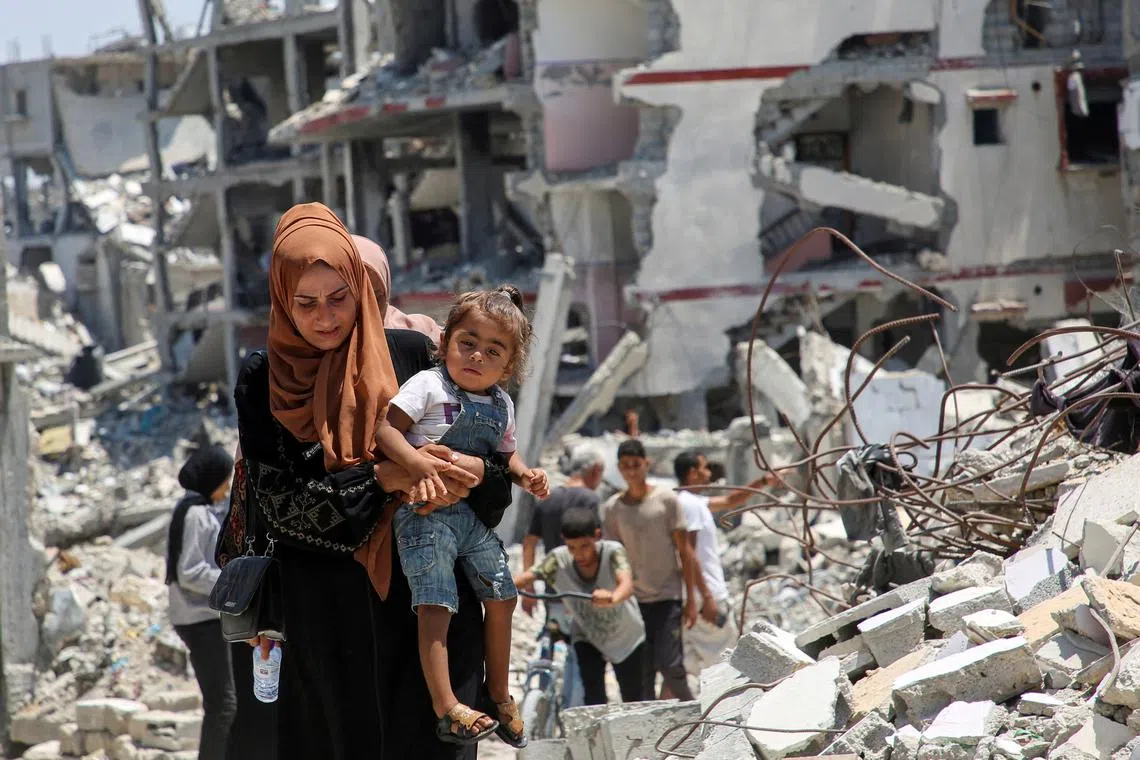 FILE PHOTO: A Palestinian woman holds her daughter as she walks past the rubble of houses destroyed during the Israeli military offensive, amid Israel-Hamas conflict, in Khan Younis in the southern Gaza Strip July 10, 2024. REUTERS/Hatem Khaled/File Photo