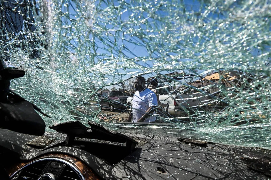 A man man walking past the shattered windshield of a car as he clears a damaged house in Rolling Fork, Mississippi, after a tornado touched down in the area, on March 26. Mississippi started clean-up operations after a destructive tornado tore across the state, killing at least 25, shredding houses and largely wiping out the small town of Rolling Fork. 